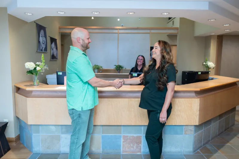 Patient shaking hands with a smiling team member at the front desk
